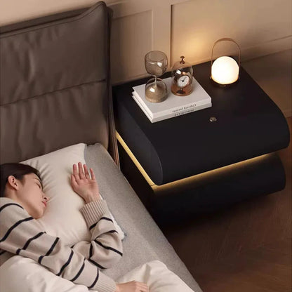 Aura Smart LED luxury nightstand in black with warm LED strip glow beside a sleeping model in a cozy luxury bedroom styled with a portable lamp, hourglass, and clock — LivDecor
