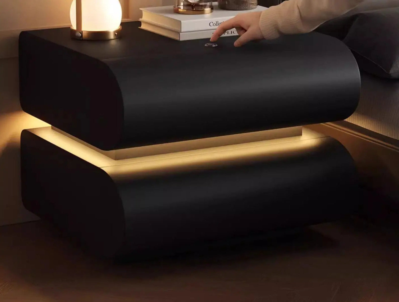 Aura Smart LED luxury nightstand in black with warm LED strip glow between tiers and model pressing touch button on top in a moody bedroom setting — LivDecor
