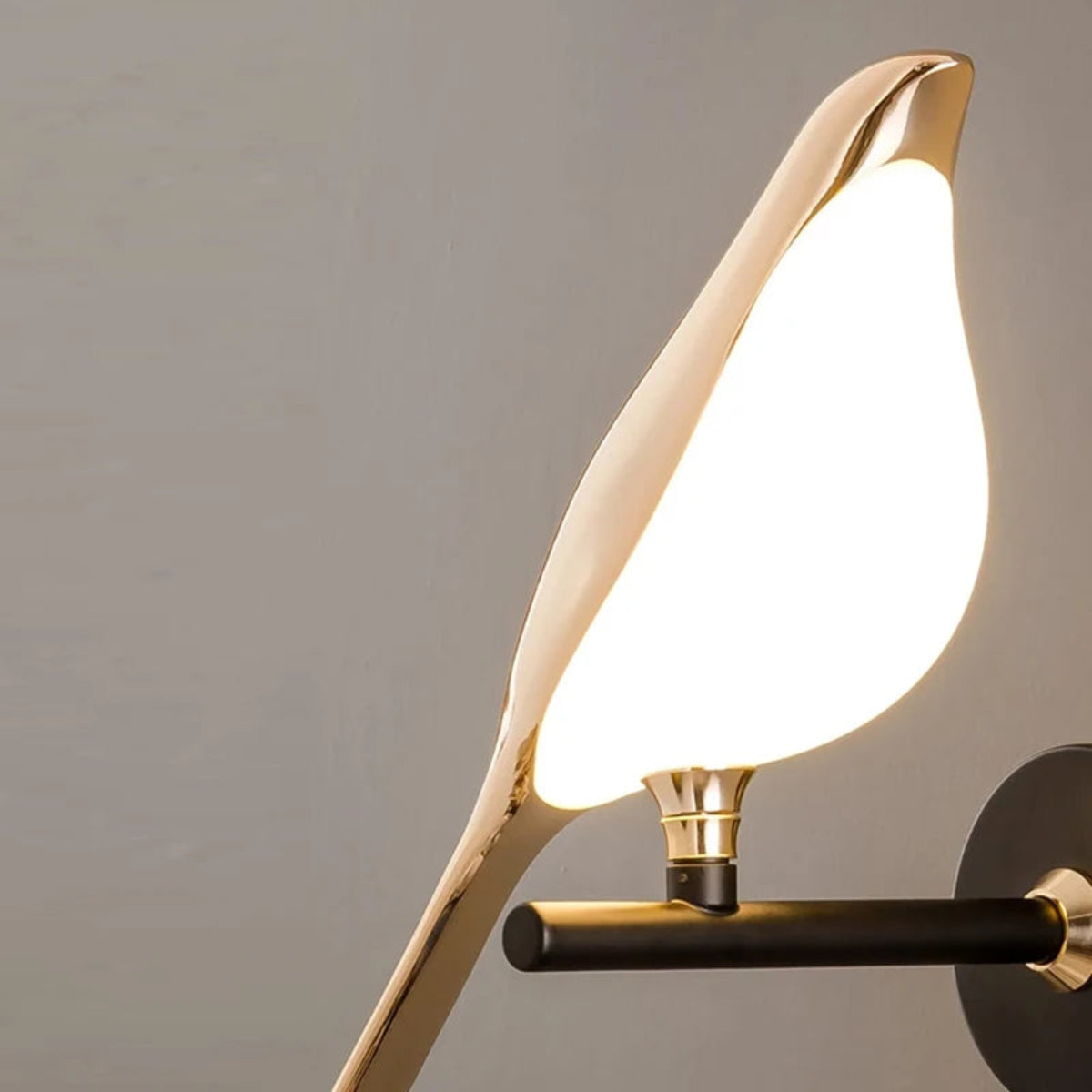 Avis Modern Origami Bird LED wall sconce close-up of single bird illuminated showing glowing frosted white body, mirror gold shell, and gold trumpet pivot connector on matte black arm against soft grey wall — LivDecor
