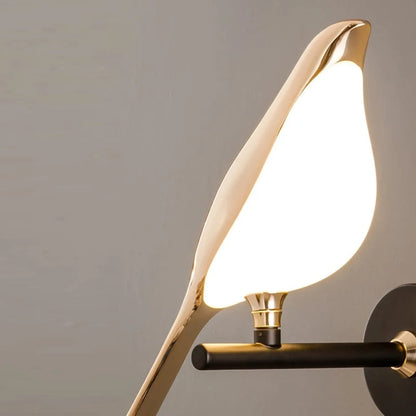Avis Modern Origami Bird LED wall sconce close-up of single bird illuminated showing glowing frosted white body, mirror gold shell, and gold trumpet pivot connector on matte black arm against soft grey wall — LivDecor
