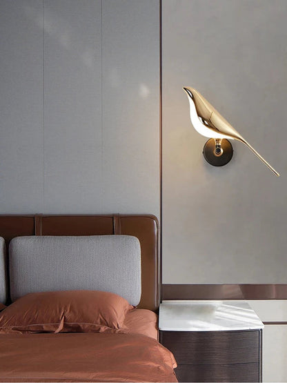 Avis Modern Origami Bird LED wall sconce in gold and matte black single-bird configuration illuminated on a soft grey panel wall beside a cognac leather bed frame with terracotta linen and marble-top walnut nightstand — LivDecor