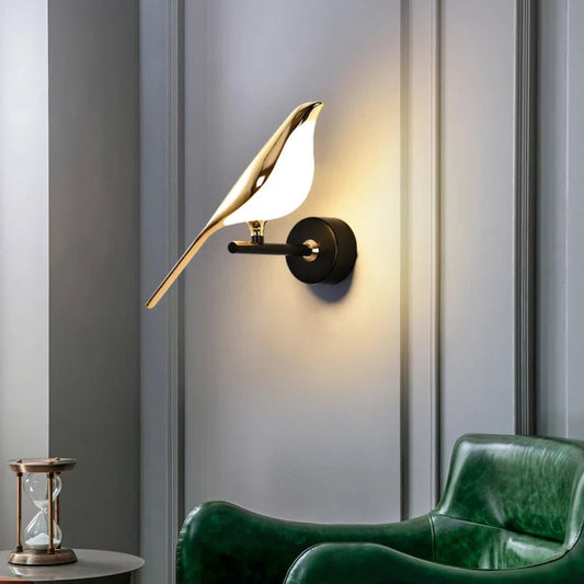 Avis Modern Origami Bird LED wall sconce in gold and matte black single-bird configuration illuminated on a soft grey panelled wall beside a deep green leather lounge chair with brass hourglass on side table — LivDecor
