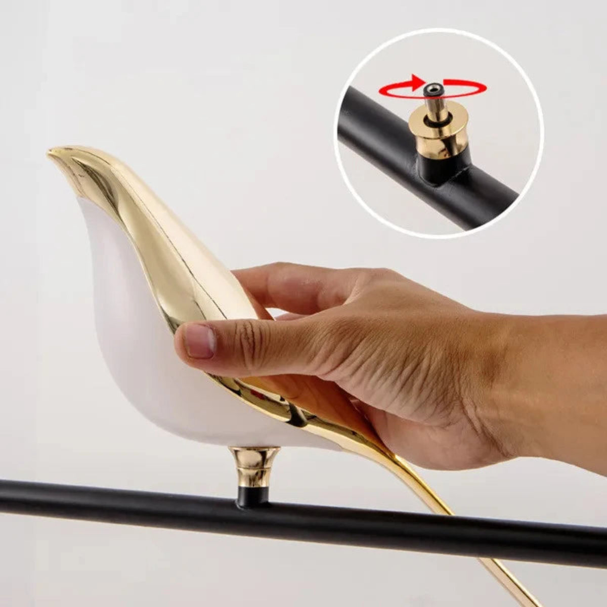 Avis Modern Origami Bird LED wall sconce hand rotating the gold bird body on the matte black arm with inset close-up showing the gold pivot screw rotation mechanism — LivDecor