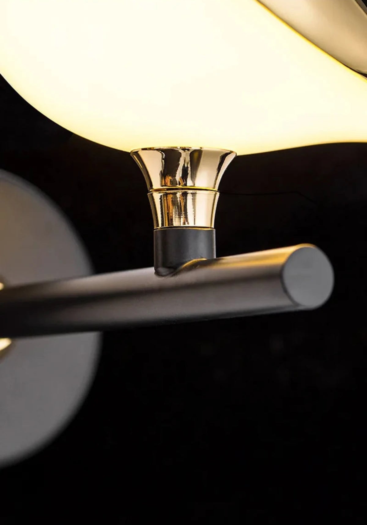 Avis Modern Origami Bird LED wall sconce extreme close-up of polished gold trumpet-shaped pivot connector joining the bird body to the matte black arm with warm ambient glow — LivDecor
