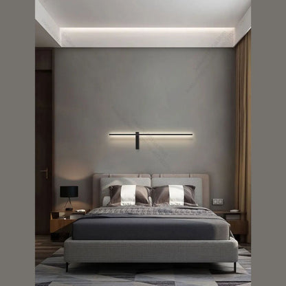 Black linear LED wall sconce mounted horizontally above a bed in a minimalist neutral-toned bedroom with warm ambient lighting — LivDecor
