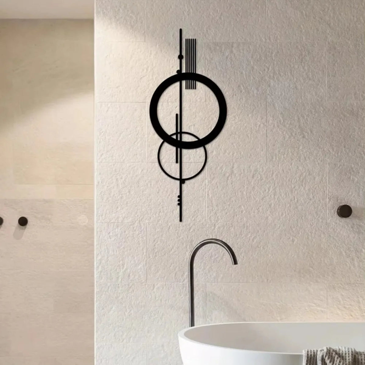 Black metal geometric abstract wall art with double circle and vertical line design mounted on a travertine tile wall in a luxury spa bathroom with a freestanding tub and matte black fixtures — LivDecor
