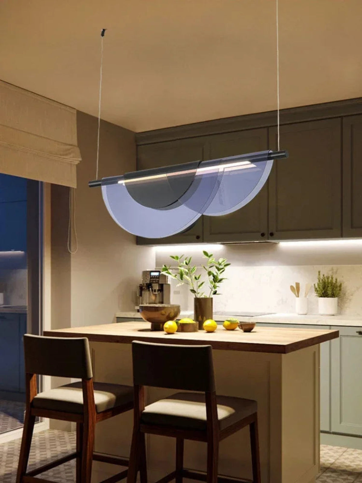 Blue acrylic petal pendant light illuminated above a wooden kitchen island with sage green cabinets, warm under-cabinet lighting, and fresh lemons styled on the counter — LivDecor