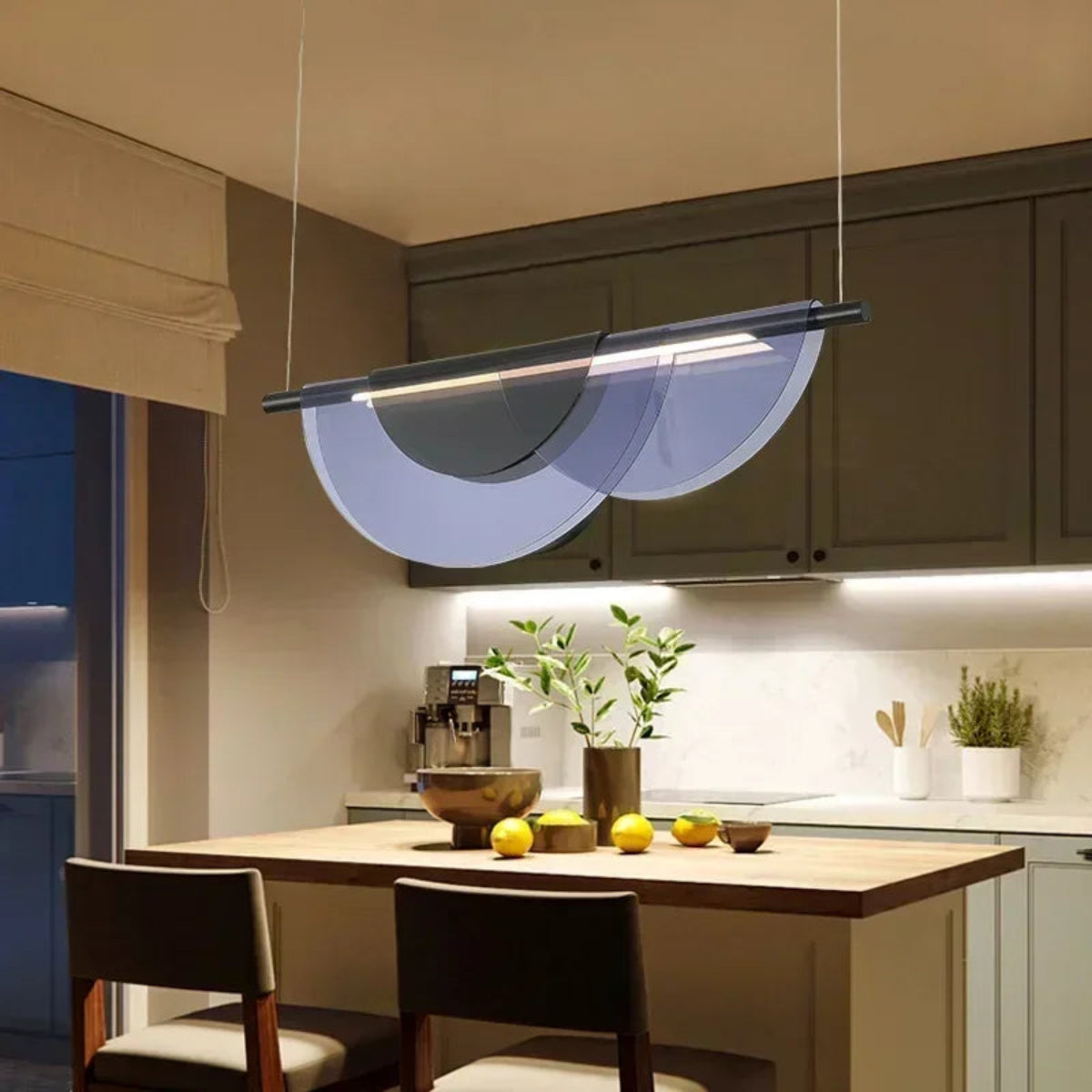 Blue acrylic petal pendant light illuminated above a wooden kitchen island with sage green cabinets, lemons, and potted plants styled on the counter in warm evening light — LivDecor