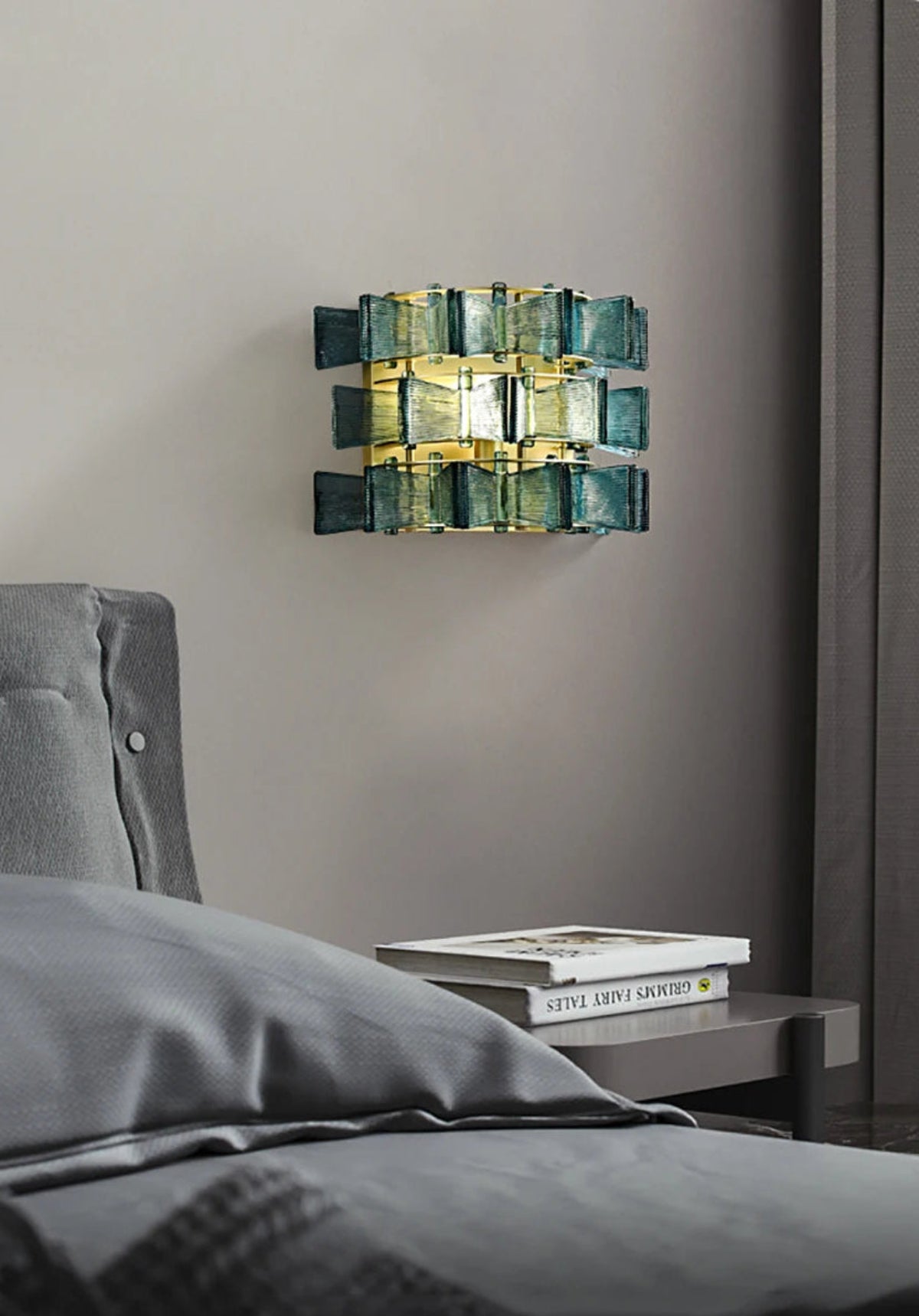 Blue ribbed glass iron wall sconce with gold frame mounted above a bedside table with stacked books in a modern grey bedroom — LivDecor
