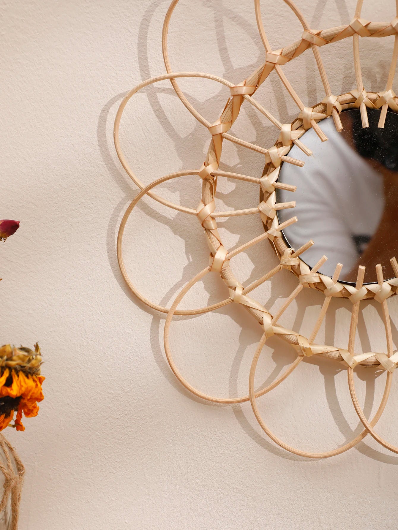 Angled close-up of boho rattan sunflower wall mirror showing woven natural cane petal detail, with dried sunflowers in a jute-wrapped vase in the foreground — LivDecor