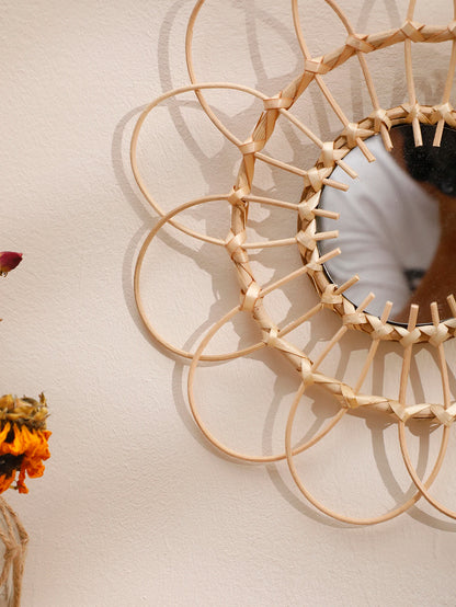 Angled close-up of boho rattan sunflower wall mirror showing woven natural cane petal detail, with dried sunflowers in a jute-wrapped vase in the foreground — LivDecor