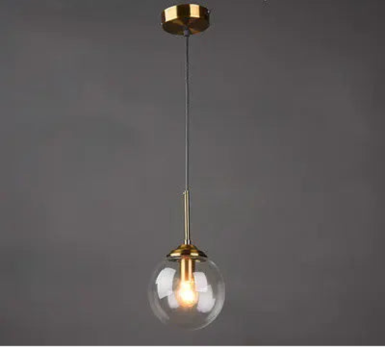 Single clear glass globe pendant light on gold cord with round ceiling canopy against a dark grey background — LivDecor
