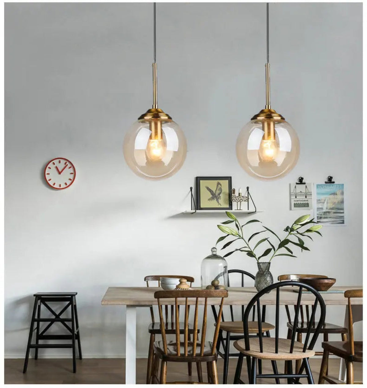 Two clear glass globe pendant lights with gold hardware hanging above a rustic wood dining table with mixed chairs in a bright casual dining room — LivDecor