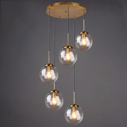 Clear glass globe pendant light, 5-light drop configuration in a staggered spiral cluster on gold cords from a round ceiling mount, lit against a dark grey background — LivDecor
