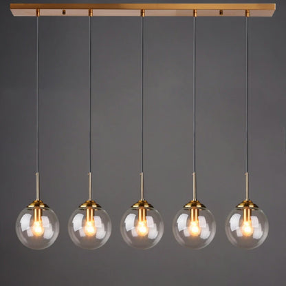 Clear glass globe pendant light, 5-light linear configuration evenly spaced on gold cords from a gold bar mount, lit against a dark grey background — LivDecor
