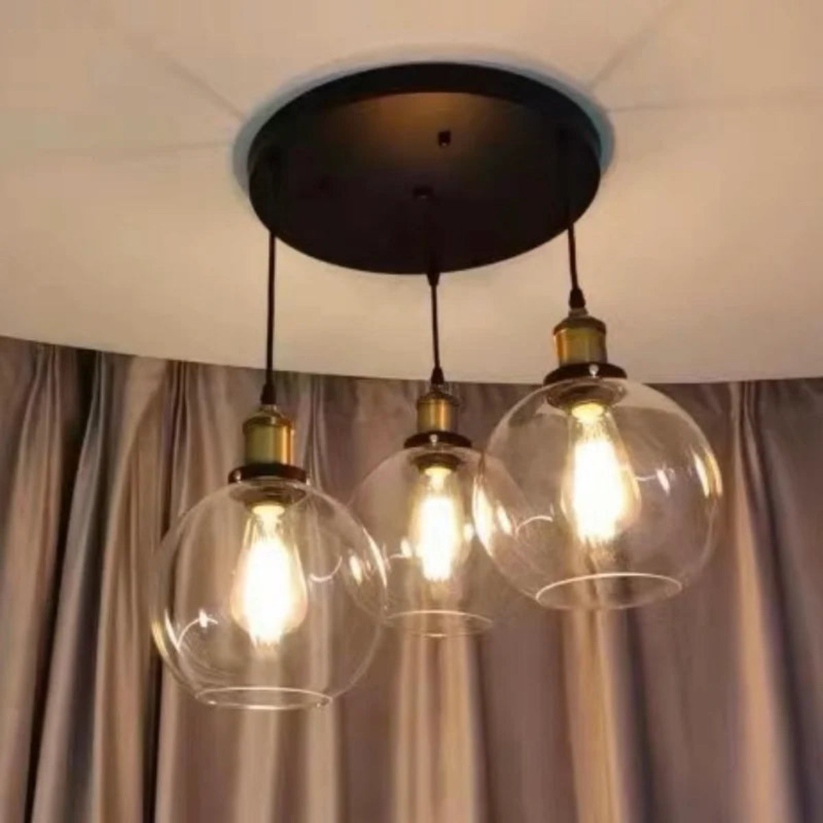 Three clear glass globe pendant lights with brass fittings hung at staggered heights from a black round ceiling plate in a real home installation — LivDecor
