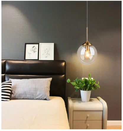 Single clear glass globe pendant light with gold hardware used as a bedside pendant beside a leather headboard against a dark grey wall in a modern bedroom — LivDecor
