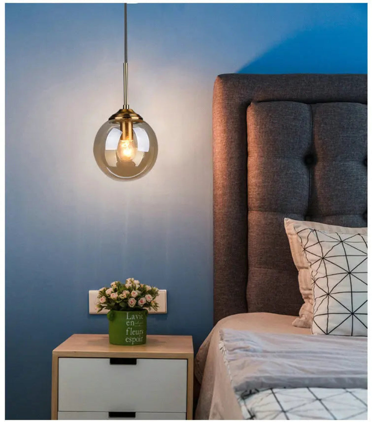 Single clear glass globe pendant light with gold hardware used as a bedside pendant beside a grey tufted headboard against a blue ombre wall — LivDecor

