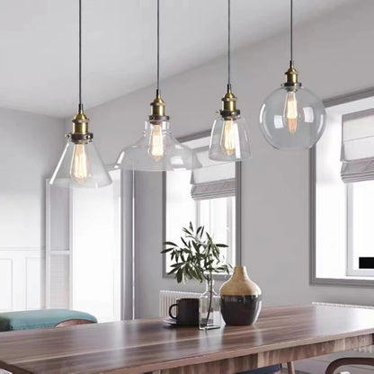 Four clear glass pendant lights in cone, bell, dome and globe shapes with brass fittings and Edison filament bulbs above a wooden dining table in a modern neutral interior — LivDecor
