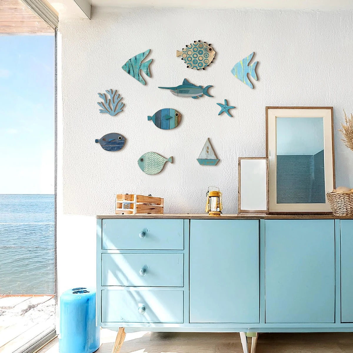 10-piece coastal wooden wall art set with hand-painted fish, swordfish, coral, starfish, and sailboat displayed above a blue sideboard in a bright beach-inspired room — LivDecor