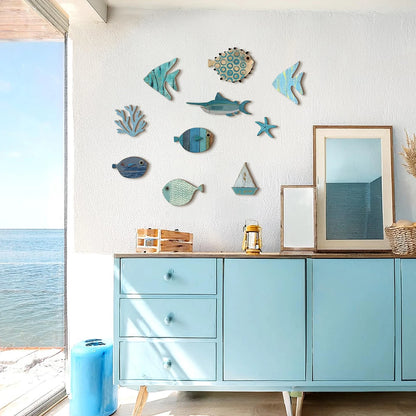 10-piece coastal wooden wall art set with hand-painted fish, swordfish, coral, starfish, and sailboat displayed above a blue sideboard in a bright beach-inspired room — LivDecor