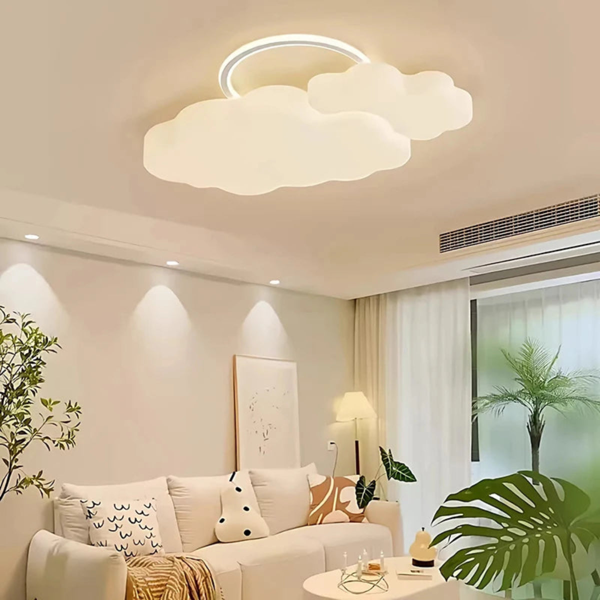 Cumulus Luxe cream sculptural cloud LED ceiling light with halo ring in a warm living room with cream sofa, tropical plants, recessed lighting, and sheer curtains — LivDecor
