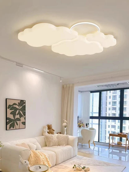 Cumulus Luxe cream sculptural cloud LED ceiling light with halo ring glowing soft white in a bright Japandi-style living room with white sofa, plush chair, botanical wall art, and floor-to-ceiling windows — LivDecor
