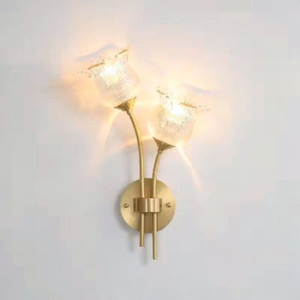 Flora Luxe botanical brass double-head wall sconce with clear ribbed floral glass shades illuminated against a white wall, angled right — LivDecor
