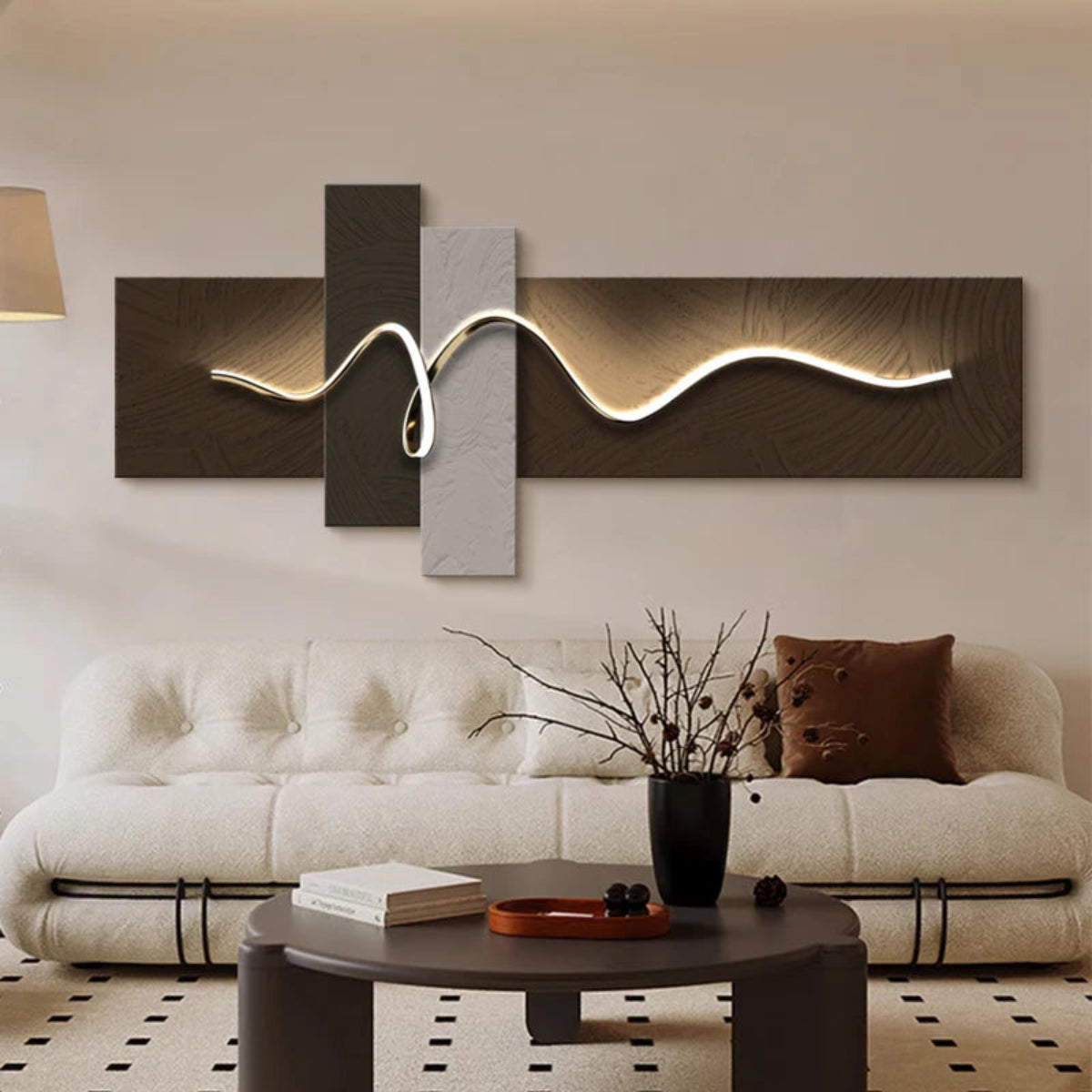 Geometric Wave LED wall art with dark walnut and silver cross-panel canvas and sinuous chrome LED light strip illuminated above a cream boucle sofa with dark coffee table and branch vase in a living room — LivDecor

