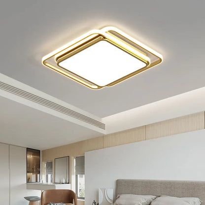 Halo modern tricolor LED flush mount ceiling light in golden square frame glowing warm white in an open-plan bedroom with cove ceiling lighting, leather chair, and neutral wood tones — LivDecor

