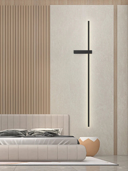Minimalist linear LED wall sconce in matte black mounted on a white plaster panel beside a cream upholstered bed with a warm wood slat feature wall in a luxury bedroom lifestyle shot — LivDecor

