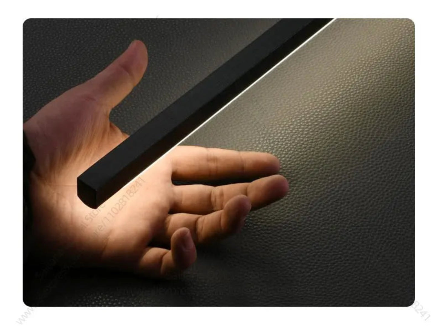 Hand holding the slim matte black bar of a minimalist linear LED wall sconce to show scale and profile against a dark textured background — LivDecor
