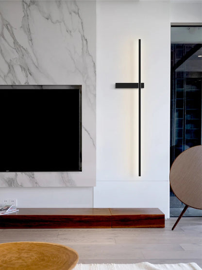 Minimalist linear LED wall sconce in matte black mounted on a white wall beside a marble TV feature wall and walnut media console in a modern living room lifestyle shot — LivDecor
