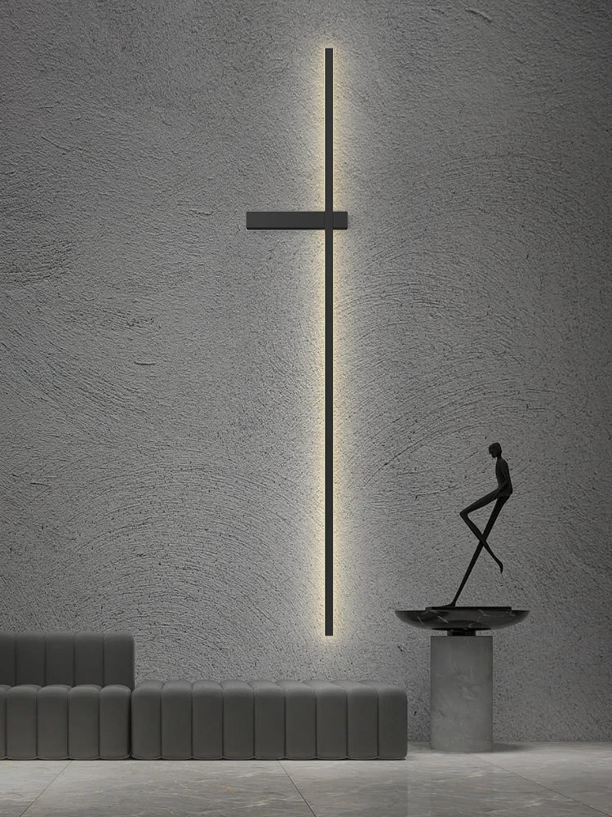 Tall minimalist linear LED wall sconce in matte black mounted on a textured concrete wall beside a bronze sculpture and modular grey sofa in a luxury living space lifestyle shot — LivDecor
