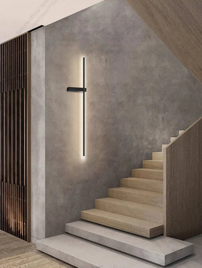 Minimalist linear LED wall sconce in matte black mounted on a concrete wall beside a modern wood staircase emitting warm white light lifestyle shot — LivDecor
