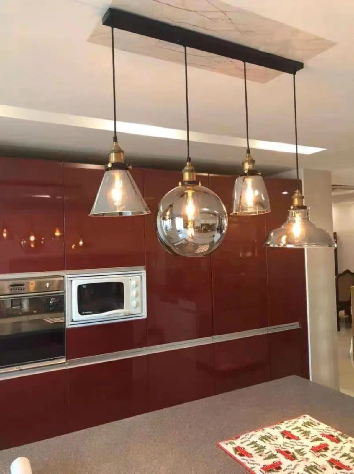 Four mixed glass pendant lights in cone, globe, bell and dome shapes hung from a black long bar ceiling plate above a kitchen island in a real home installation — LivDecor