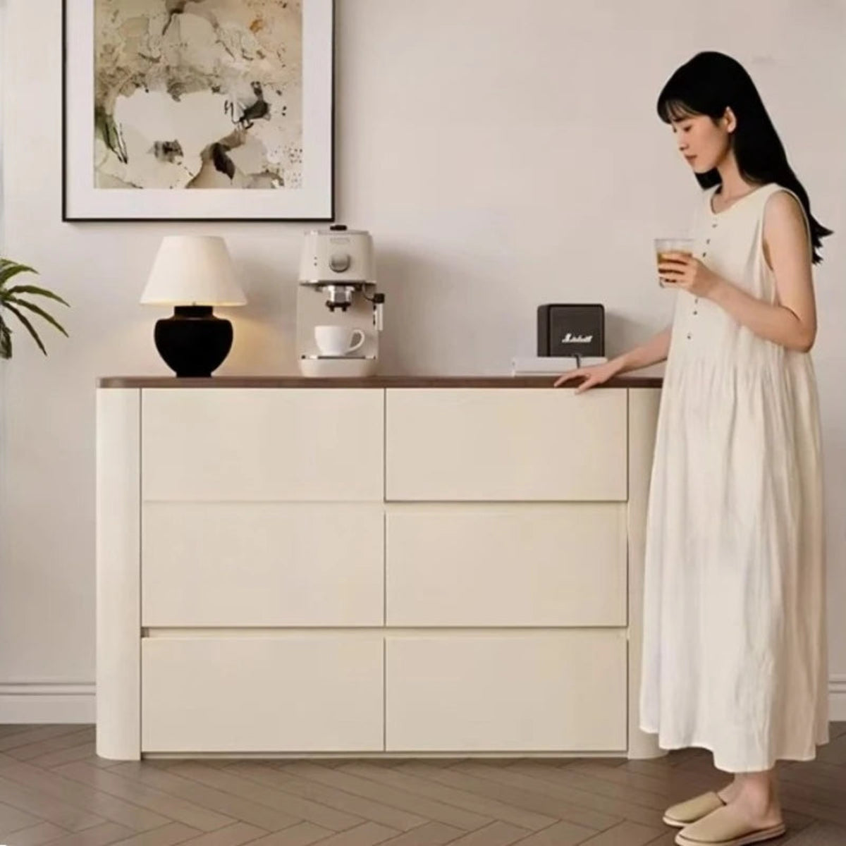 Nordic Elegance cream ivory buffet credenza with walnut top shown with a female model in a white dress holding coffee in a wide lifestyle shot with abstract art and palm plant — LivDecor
