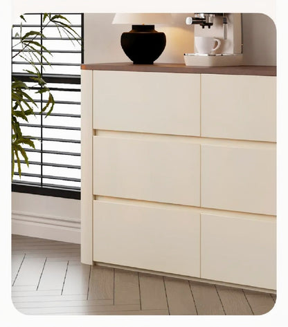Nordic Elegance credenza detail showing cream handleless grooved drawer fronts, walnut top edge and rounded corner beside a window with a plant — LivDecor
