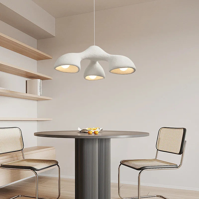 Odense Cocoon sculptural cloud pendant chandelier in white 3-head downward configuration hanging over a fluted dark round dining table with cane Cesca chairs and open wood shelving — LivDecor
