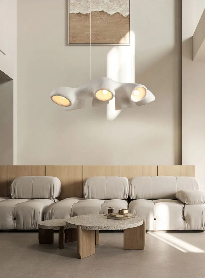 Odense Cocoon sculptural cloud pendant chandelier in white 3-head linear configuration hanging in a double-height luxury living room with modular bouclé sofa, travertine coffee tables, and abstract art — LivDecor