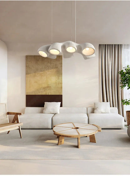 Odense Cocoon sculptural cloud pendant chandelier in white 3-head linear configuration hanging in a warm neutral living room with gold abstract art, white modular sofa, and rattan coffee table — LivDecor
