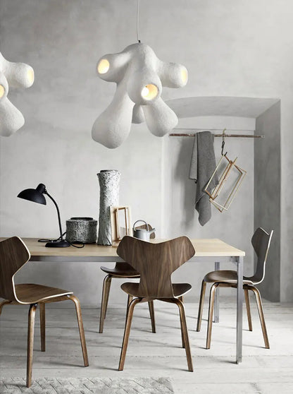 Two Odense Cocoon sculptural cloud pendant chandeliers in white 4-head configuration hung at staggered heights over a wood dining table with walnut Grand Prix chairs in a Scandinavian concrete dining room — LivDecor
