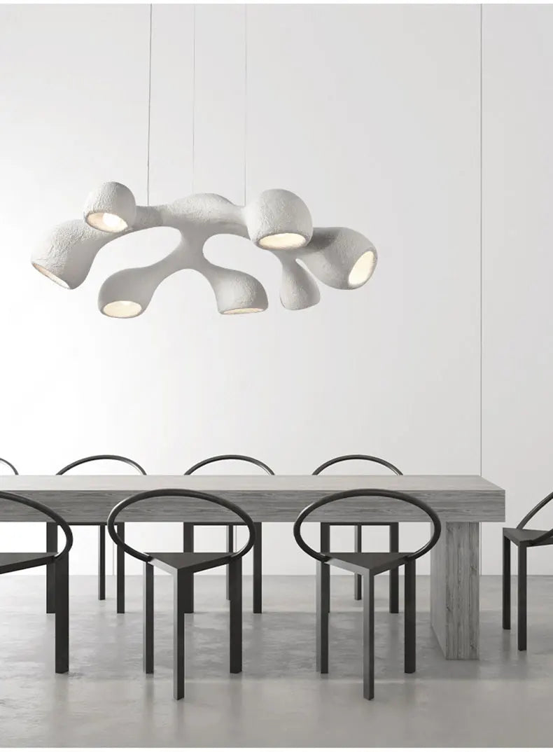 Odense Cocoon sculptural cloud pendant chandelier in white 7-head configuration hanging over a long concrete dining table with black loop chairs in a minimalist white dining room — LivDecor
