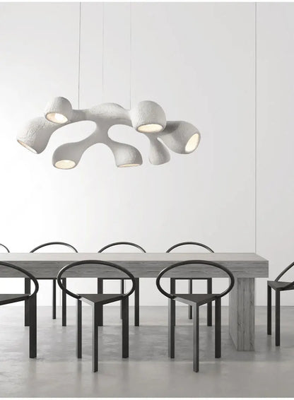 Odense Cocoon sculptural cloud pendant chandelier in white 7-head configuration hanging over a long concrete dining table with black loop chairs in a minimalist white dining room — LivDecor
