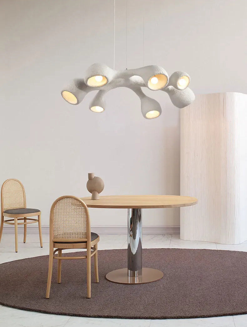 Odense Cocoon sculptural cloud pendant chandelier in white 7-head flat configuration hanging over a round oak dining table with chrome pedestal base and rattan chairs in a minimalist neutral dining room — LivDecor