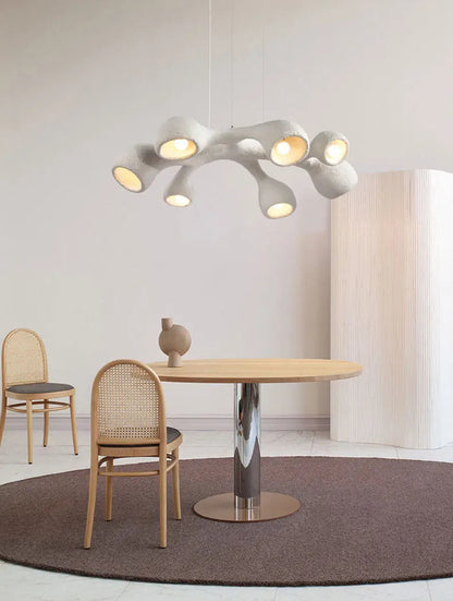 Odense Cocoon sculptural cloud pendant chandelier in white 7-head flat configuration hanging over a round oak dining table with chrome pedestal base and rattan chairs in a minimalist neutral dining room — LivDecor