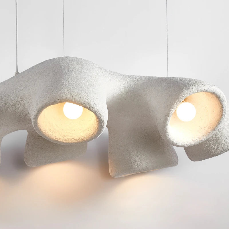 Odense Cocoon sculptural cloud pendant chandelier close-up of two lit cavities with exposed globe bulbs casting warm glow showing rich sandy pumice-like textured white surface — LivDecor
