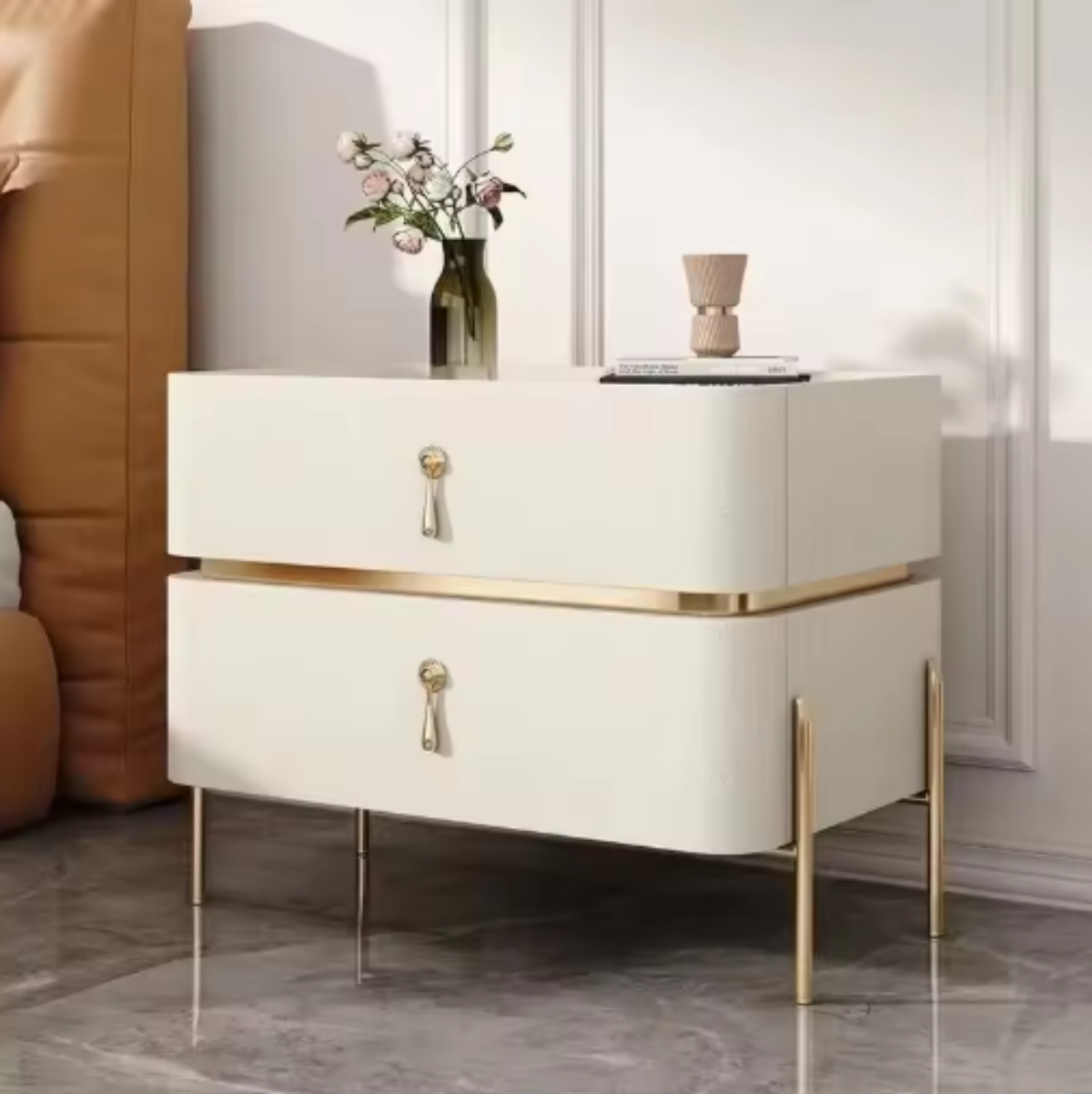 Slate top luxury beige two-drawer nightstand with gold trim, drop-pull handles and slim tapered gold legs shown at an angle beside a tan leather bed with roses — LivDecor