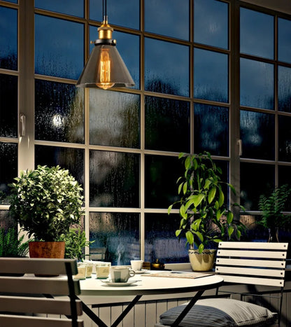 Smoke grey glass cone pendant light with brass fitting above a bistro table with steaming coffee cups and green plants against rain-streaked industrial windows at night — LivDecor