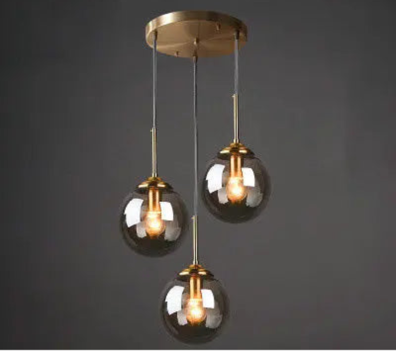 Three smoke grey glass globe pendant lights on staggered gold cords and round ceiling mount in a cluster configuration against a dark grey background — LivDecor
